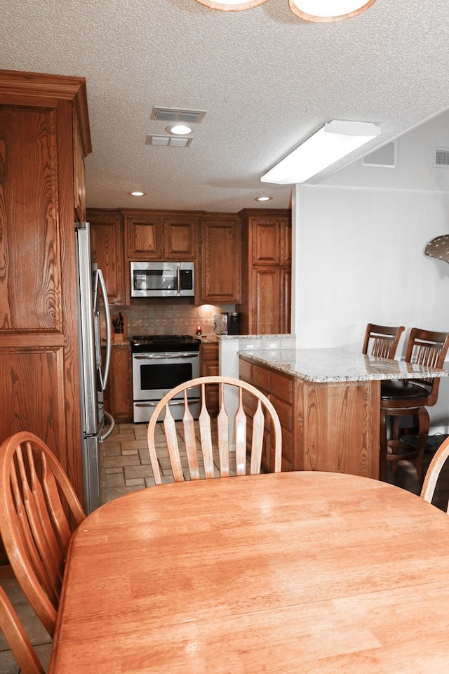 kitchen featuring stainless steel appliances, light stone counters, a textured ceiling, and decorative backsplash