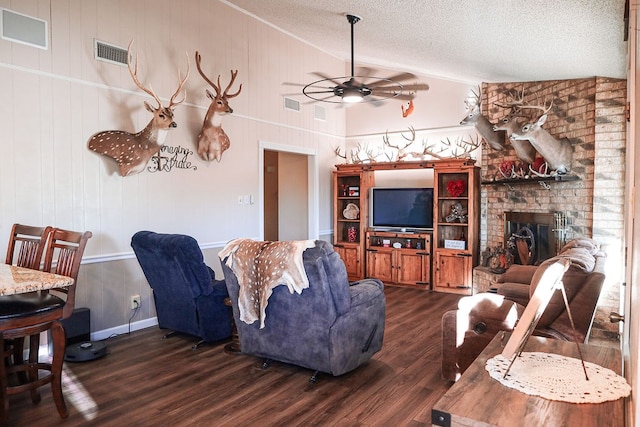 living room with dark hardwood / wood-style floors, a fireplace, lofted ceiling, ceiling fan, and a textured ceiling