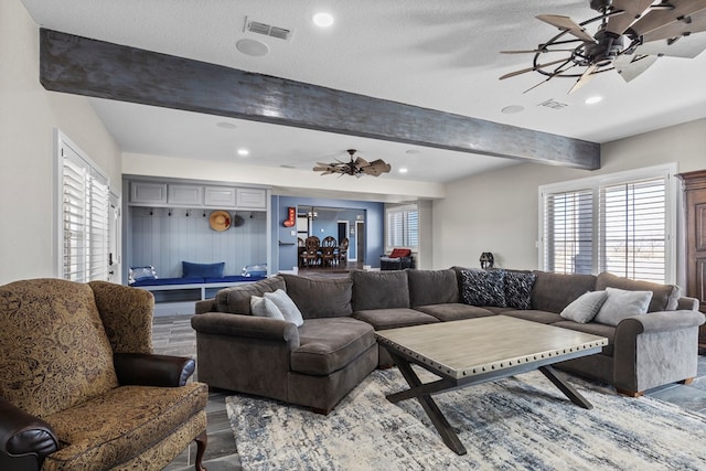 living room with ceiling fan, a textured ceiling, and beamed ceiling