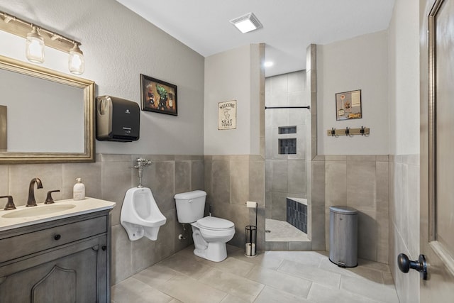 bathroom featuring a tile shower, vanity, tile walls, and toilet