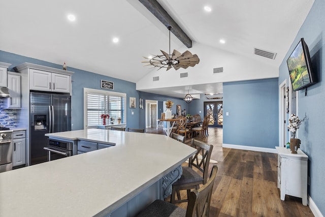 kitchen featuring lofted ceiling with beams, hanging light fixtures, a kitchen breakfast bar, stainless steel appliances, and white cabinets