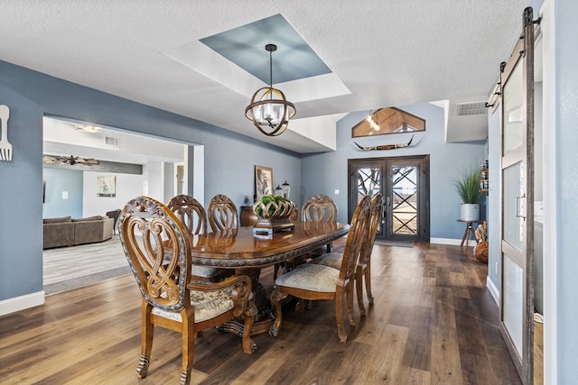 dining area featuring hardwood / wood-style flooring, an inviting chandelier, a tray ceiling, a barn door, and french doors