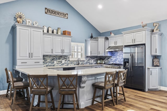 kitchen featuring vaulted ceiling, white cabinets, backsplash, stainless steel fridge, and a kitchen breakfast bar