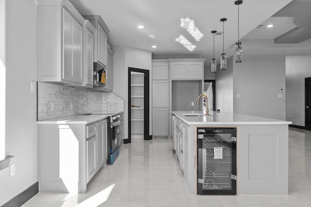 kitchen with a center island with sink, sink, appliances with stainless steel finishes, decorative light fixtures, and beverage cooler