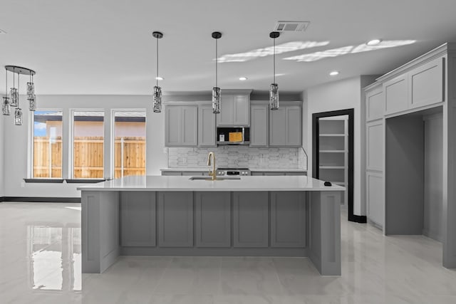 kitchen with tasteful backsplash, sink, decorative light fixtures, a center island with sink, and gray cabinets