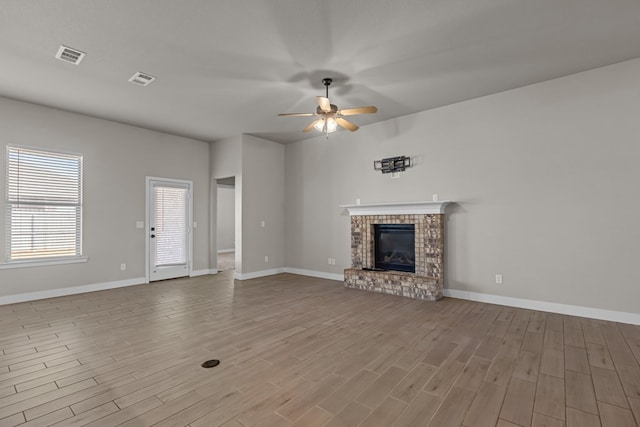 unfurnished living room with ceiling fan, wood finished floors, visible vents, baseboards, and a brick fireplace