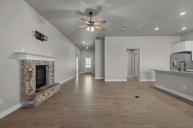 unfurnished living room featuring visible vents, baseboards, ceiling fan, light wood-style floors, and a fireplace