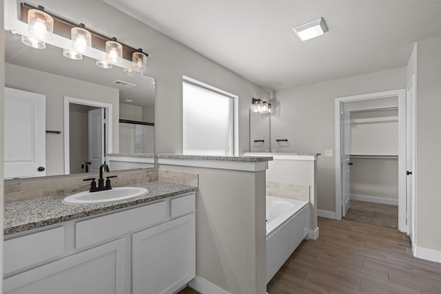 full bath featuring wood finished floors, vanity, visible vents, baseboards, and a bath