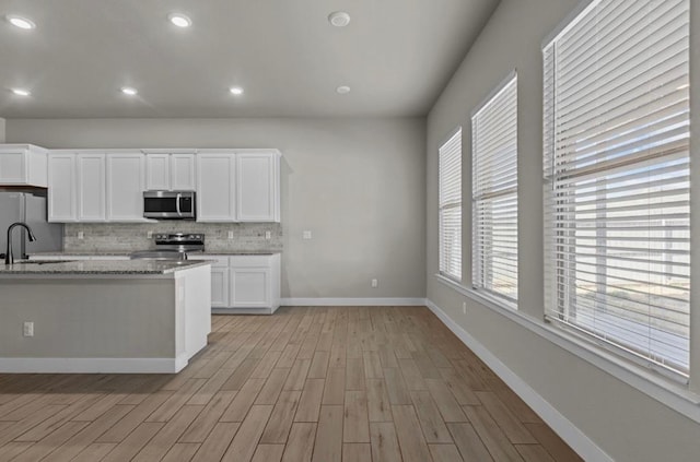 kitchen with stainless steel appliances, backsplash, light wood-style floors, white cabinetry, and light stone countertops