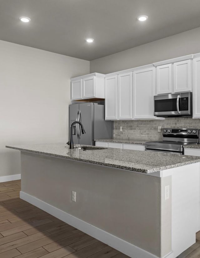 kitchen featuring stainless steel appliances, wood finished floors, a center island with sink, and white cabinets