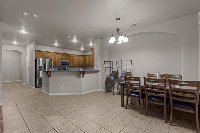 kitchen featuring light tile patterned floors, a peninsula, appliances with stainless steel finishes, and brown cabinets