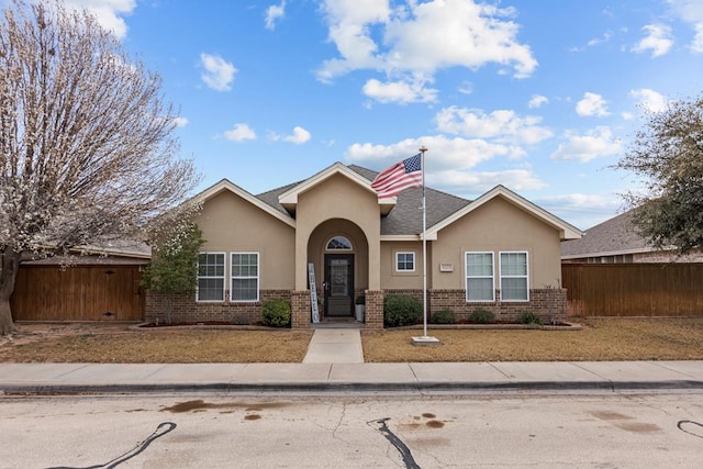 view of front of property featuring a shingled roof, brick siding, fence, and stucco siding