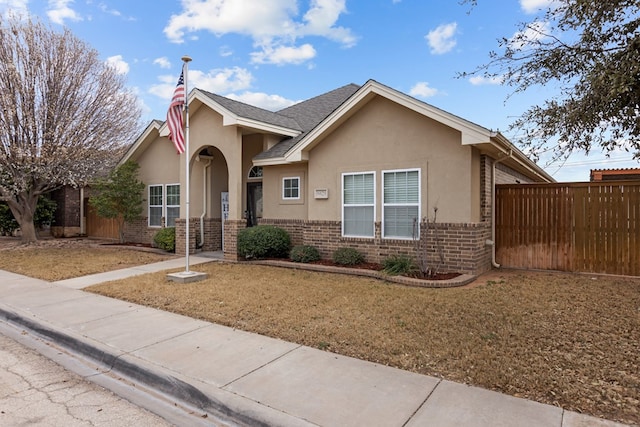 view of front of house featuring brick siding, a front lawn, fence, and stucco siding