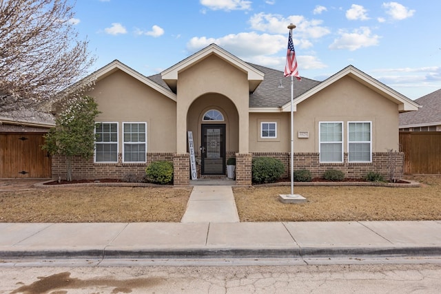 view of front of property with brick siding, a shingled roof, fence, and stucco siding