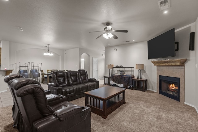 carpeted living area featuring arched walkways, visible vents, a textured ceiling, a tile fireplace, and ceiling fan with notable chandelier