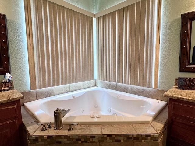 full bath featuring a whirlpool tub, vanity, and a textured wall