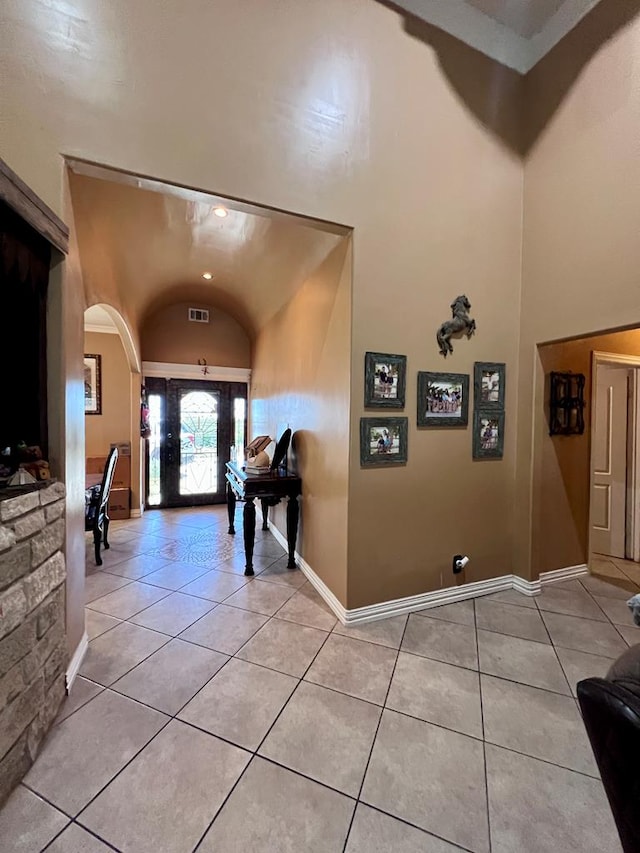 entrance foyer with high vaulted ceiling, baseboards, arched walkways, and light tile patterned flooring