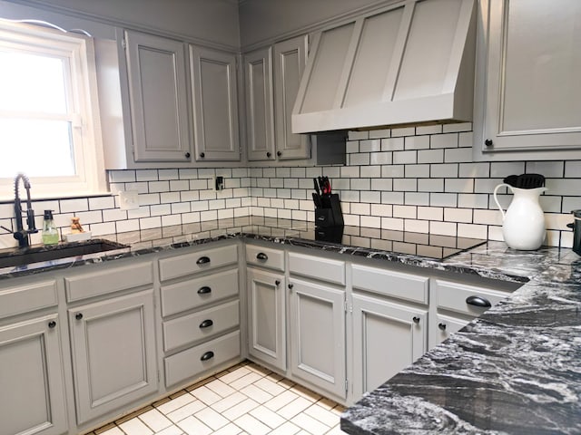 kitchen featuring premium range hood, dark stone counters, sink, and tasteful backsplash