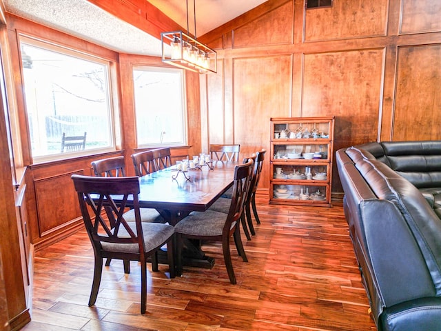 dining space with vaulted ceiling, wooden walls, and dark hardwood / wood-style flooring