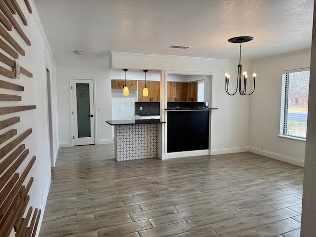 kitchen with crown molding, hardwood / wood-style flooring, an inviting chandelier, backsplash, and decorative light fixtures