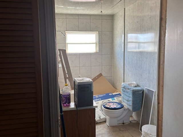 bathroom with tile patterned floors, toilet, and tile walls