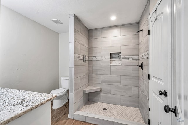 bathroom with a tile shower, hardwood / wood-style floors, and toilet