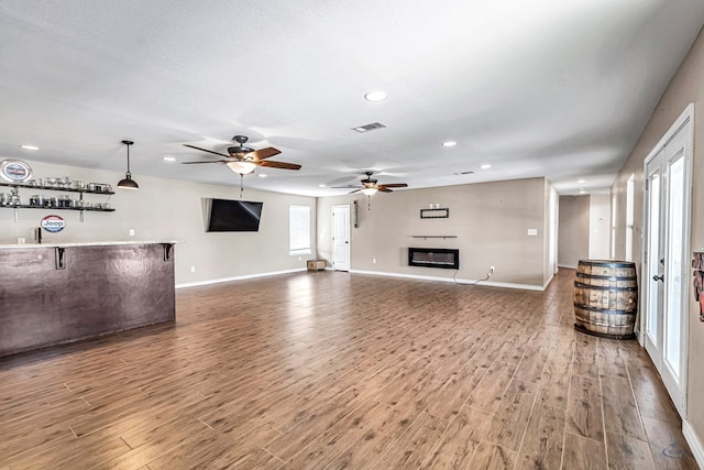 unfurnished living room featuring hardwood / wood-style floors, indoor bar, a textured ceiling, and ceiling fan