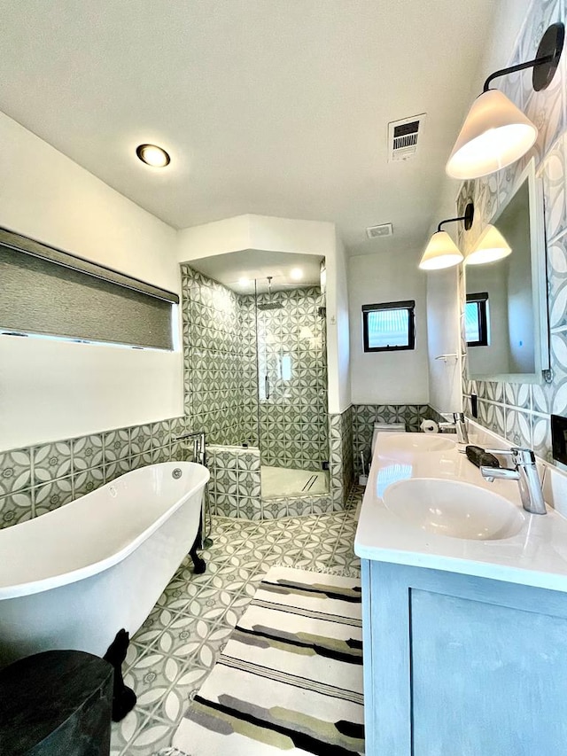 bathroom featuring visible vents, a soaking tub, double vanity, a stall shower, and a sink