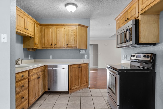 kitchen with light tile patterned floors, light countertops, appliances with stainless steel finishes, a sink, and a textured ceiling