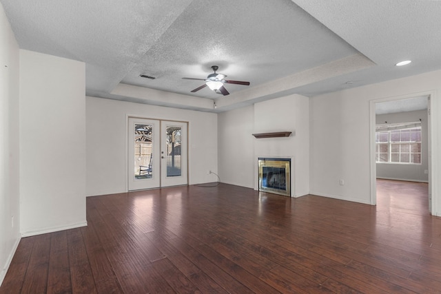 unfurnished living room with a textured ceiling, a tray ceiling, dark wood-type flooring, and a glass covered fireplace