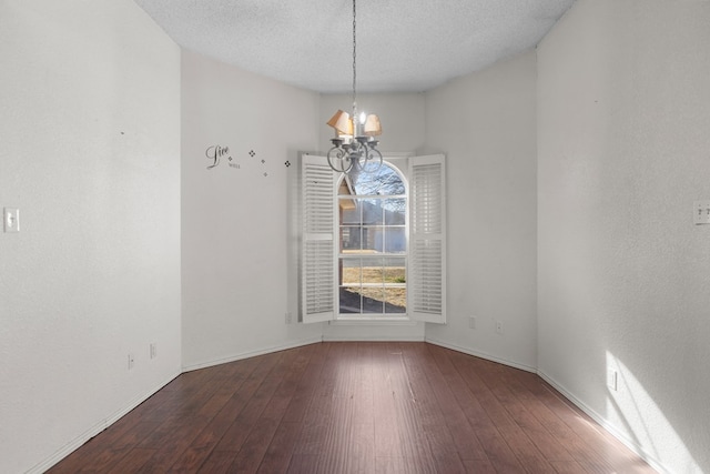 unfurnished room with a textured ceiling, baseboards, dark wood finished floors, and a notable chandelier