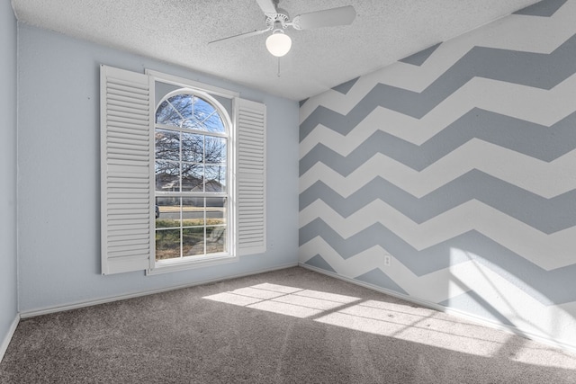 carpeted empty room with a textured ceiling, a ceiling fan, and baseboards