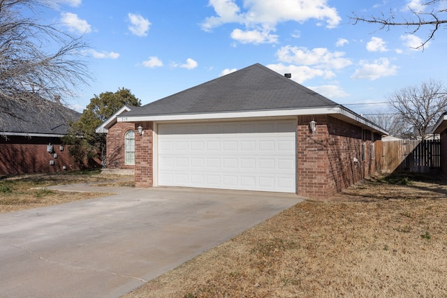 view of side of home featuring a garage, concrete driveway, roof with shingles, fence, and brick siding