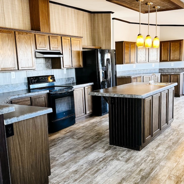 kitchen featuring sink, hanging light fixtures, black appliances, a center island with sink, and light hardwood / wood-style flooring