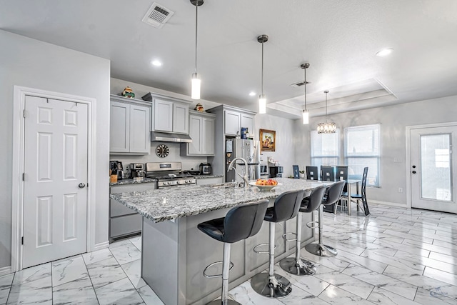 kitchen with marble finish floor, stainless steel appliances, hanging light fixtures, a kitchen island with sink, and a kitchen bar