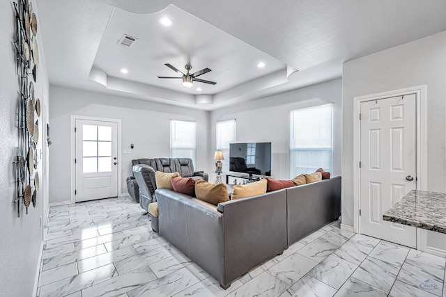 living area with marble finish floor, plenty of natural light, a raised ceiling, and visible vents