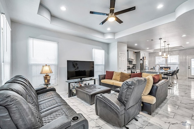 living area with recessed lighting, a raised ceiling, marble finish floor, and baseboards