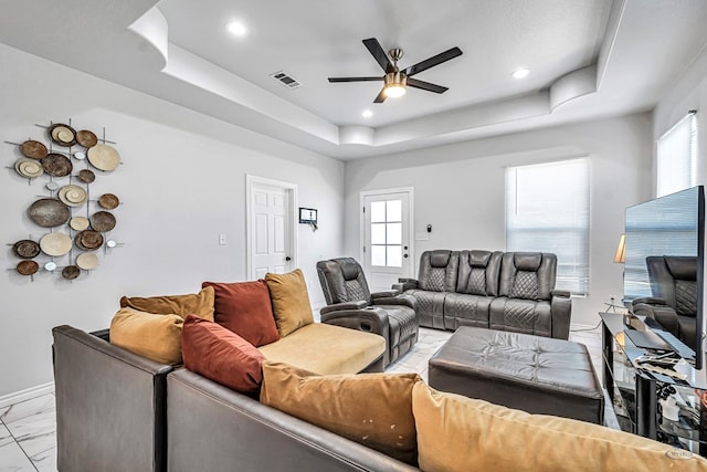 living room featuring a tray ceiling, a healthy amount of sunlight, visible vents, and ceiling fan