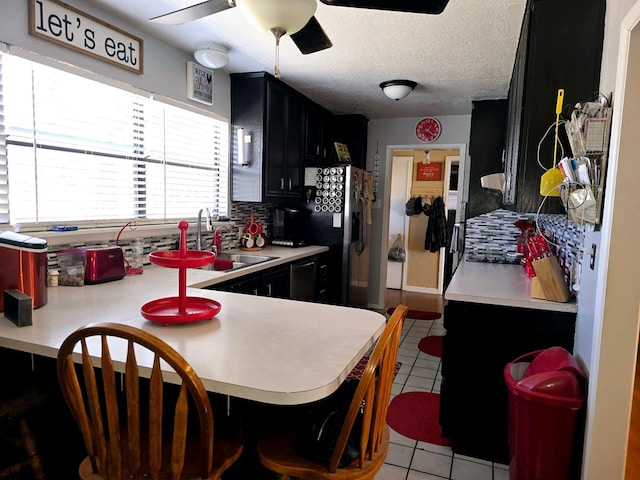 kitchen featuring light tile patterned floors, dark cabinetry, ceiling fan, and a sink