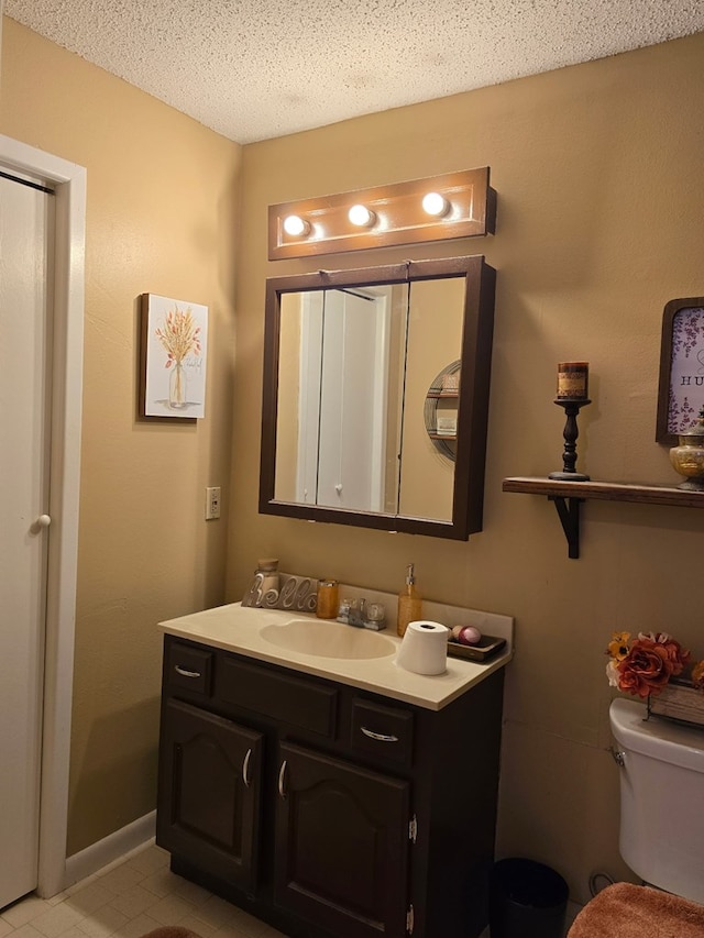 bathroom with vanity, toilet, baseboards, and a textured ceiling