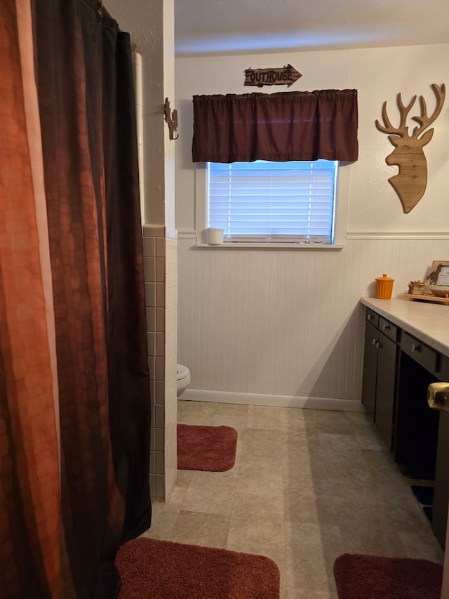 full bathroom featuring a wainscoted wall, curtained shower, toilet, and vanity