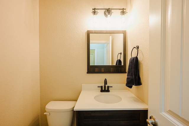 half bathroom with toilet, a textured wall, and vanity