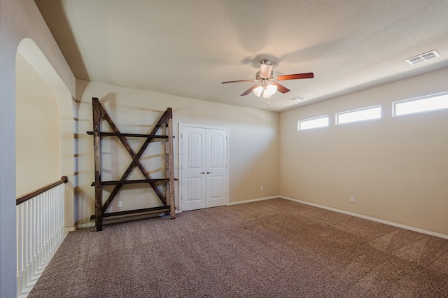 empty room with a textured ceiling, carpet, visible vents, and a ceiling fan