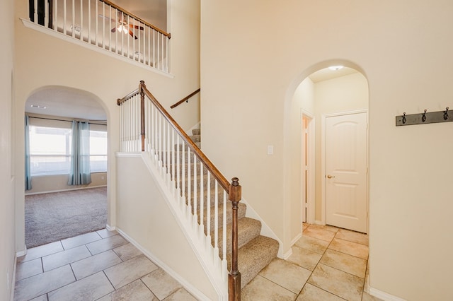 stairway with arched walkways, baseboards, carpet, tile patterned flooring, and a high ceiling