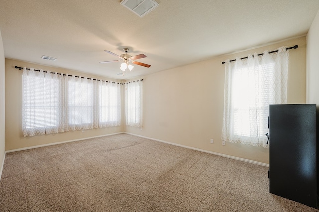 carpeted empty room with visible vents, ceiling fan, and baseboards