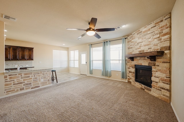 unfurnished living room with light colored carpet, visible vents, a sink, and a stone fireplace