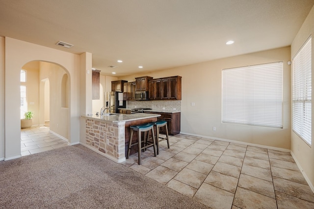 kitchen featuring visible vents, backsplash, appliances with stainless steel finishes, light tile patterned flooring, and a kitchen bar