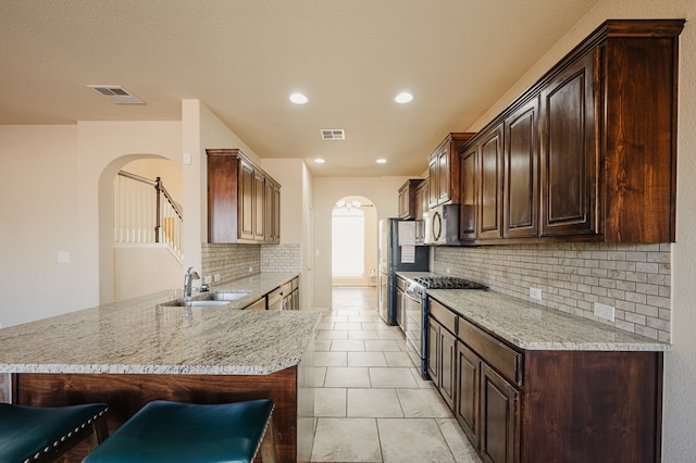 kitchen with arched walkways, a breakfast bar, a sink, visible vents, and appliances with stainless steel finishes