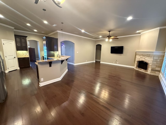 unfurnished living room with arched walkways, a stone fireplace, dark wood-style flooring, and a ceiling fan