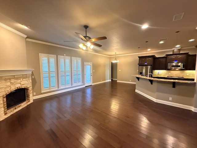 unfurnished living room with a stone fireplace, dark wood-type flooring, a ceiling fan, baseboards, and ornamental molding